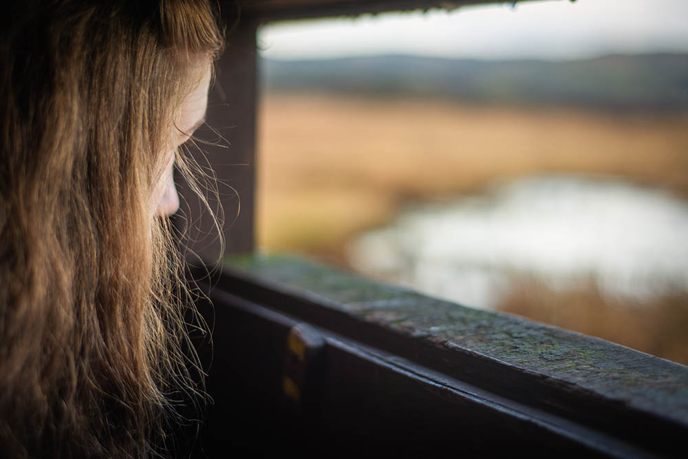 Young femal bird watcher looking out from a Hide next to a Scottish loch