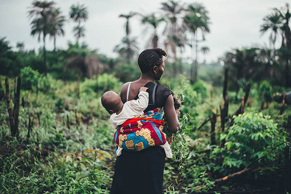 Woman carrying her child on her back whilst working in a field in Sierra Leone