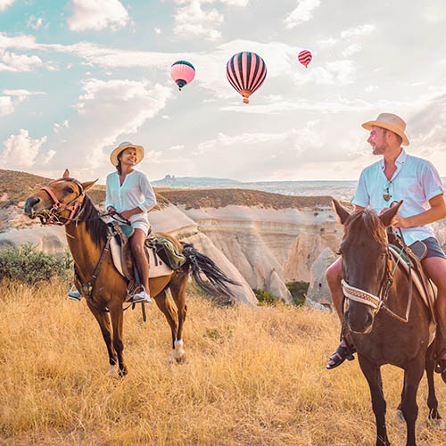 Happy young couple horse riding with hot air balloons in the background at Cappadocia, Turkey