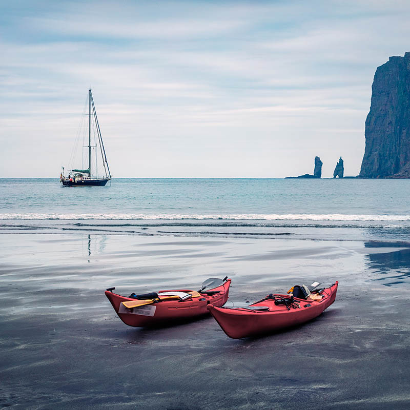 Two red canoes on the beach of Streymoy island with Eidiskollur cliffs in the background, Faroe Islands