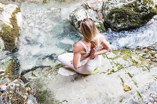 Young woman sitting on rocks by the water in a yoga position