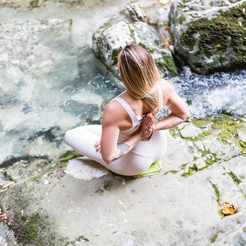 Young woman sitting on rocks by the water in a yoga position