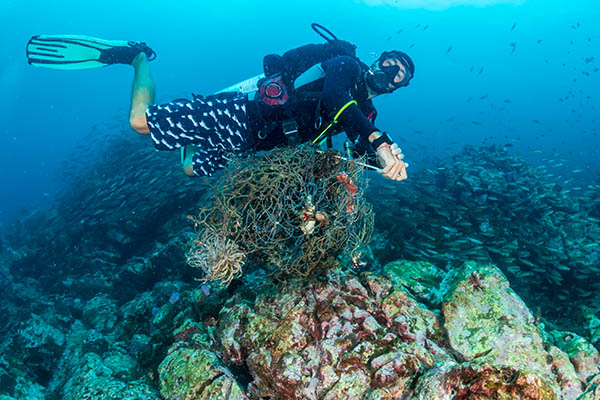 diver removing abandoned fishing net entangled on coral reef