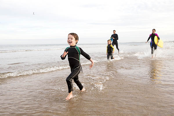 Family in wetsuits running along a beach