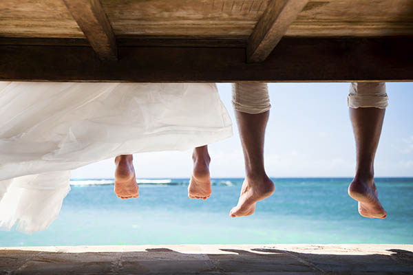 Close up of bride & grooms bare feet sitting by the ocean