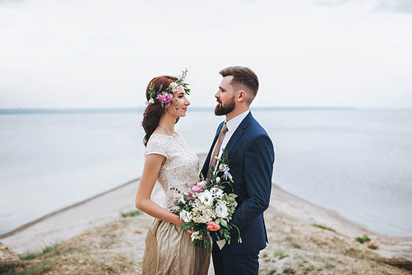 Newlyweds look into each other's eyes, standing on the river bank