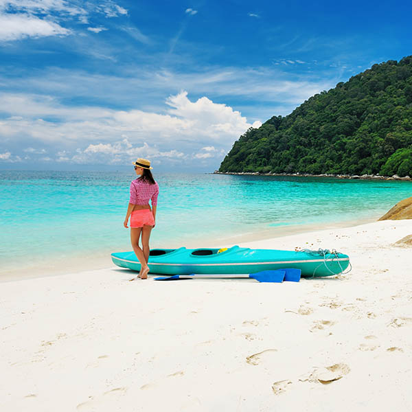 Woman standing next to a kayak on an island beach in Malaysia