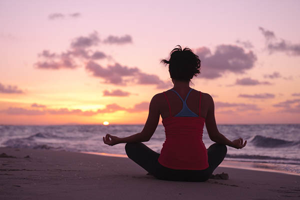 Young woman practicing yoga on a beach at sunrise