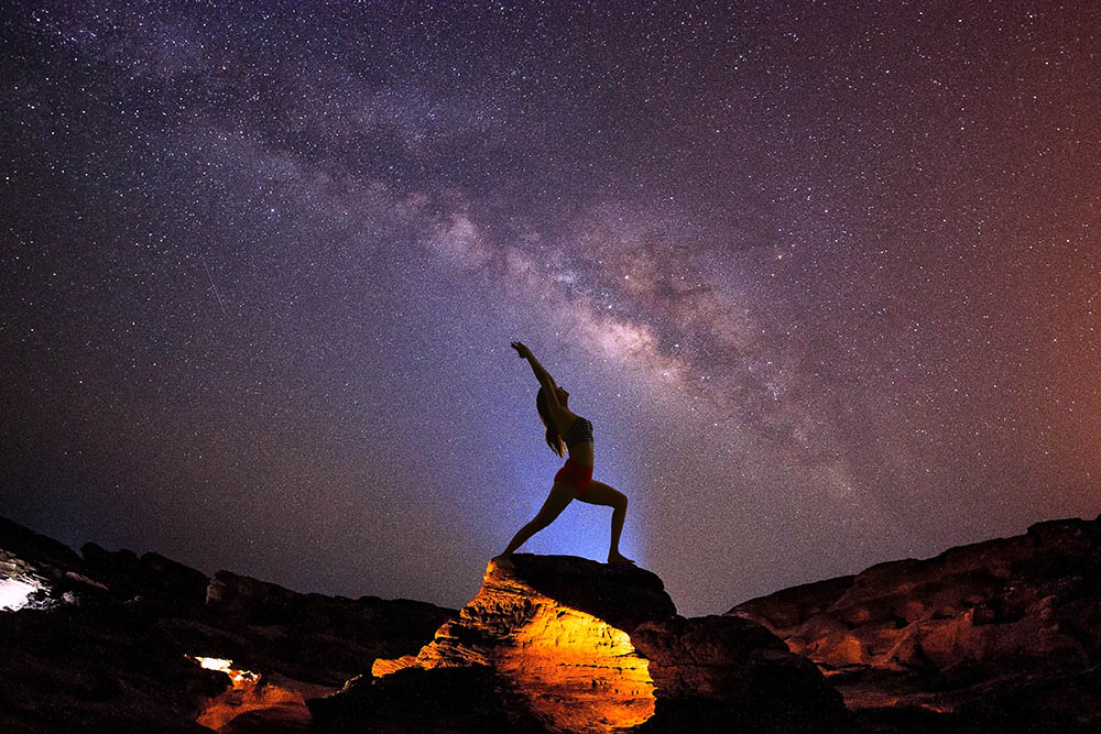 Milky Way night sky with stars and silhouette of woman practicing yoga