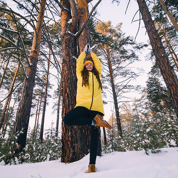 beautiful young woman in yellow jacket and hat doing workout or yoga in winter park among snow covered trees