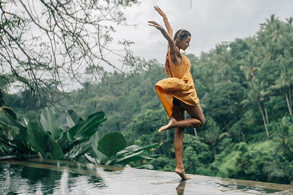 Woman in yellow dress enjoying tropical rain while standing on infinity pool