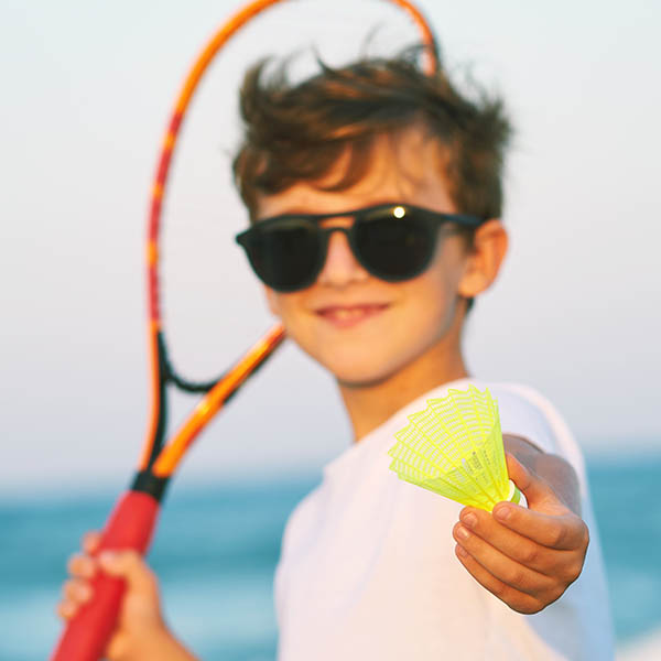 A boy wearing sunglasses plays beach tennis