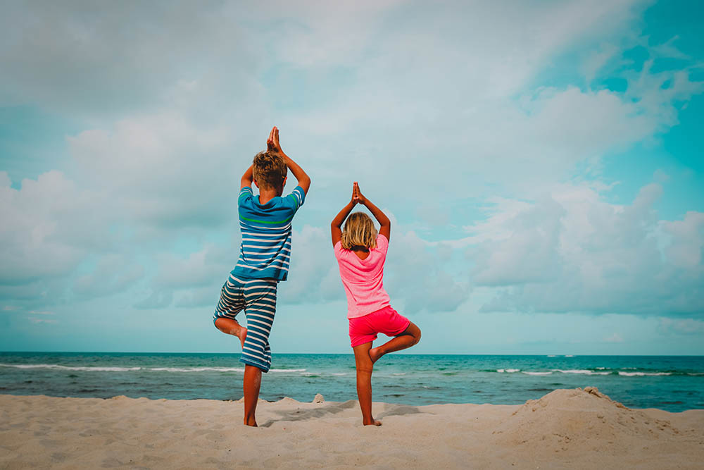 boy and girl doing yoga on a beach