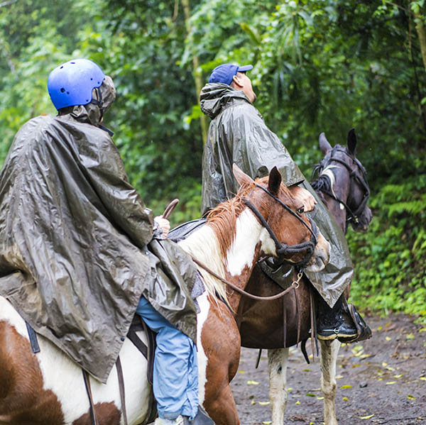 Senior woman and her gide during Horseback riding on foggy and rainy day while crossing the river Arenal near small town La Fortuna in Costa Rica