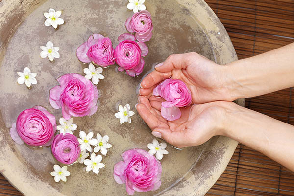 Close up of woman's hands holding pink flower in a spa bath