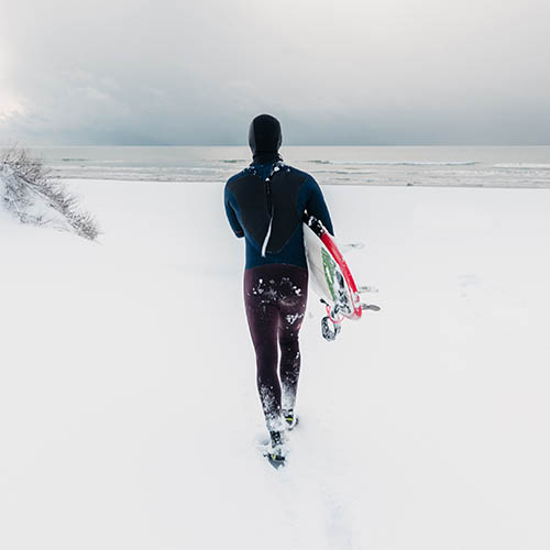 Surfer in wetsuit with surfboard heading to the ocean on a snowy day