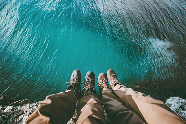 Close up of a couple's feet sitting on a cliff above the sea