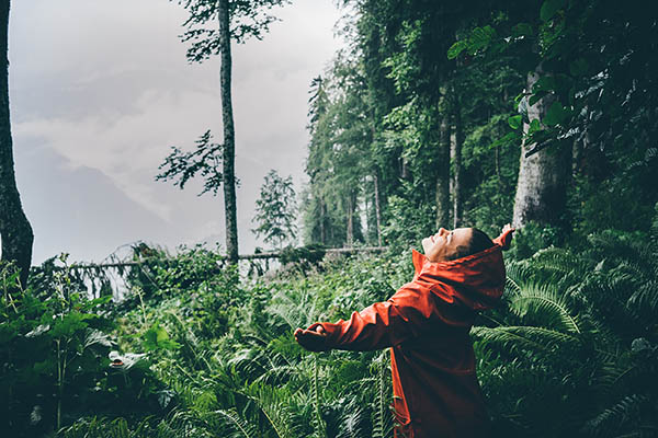 Young woman in an orange raincoat enjoying warm summer rain in a tropical forest