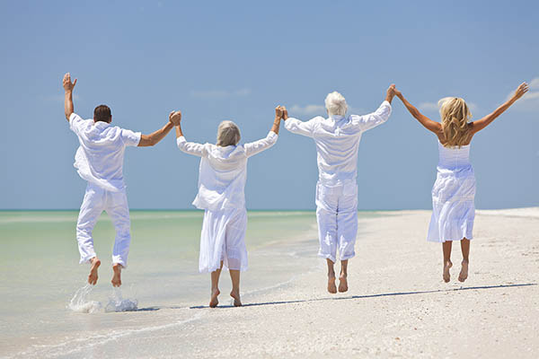 Back view of a senior couple and a younger couple dressed in white jumping on a beach next to the sea