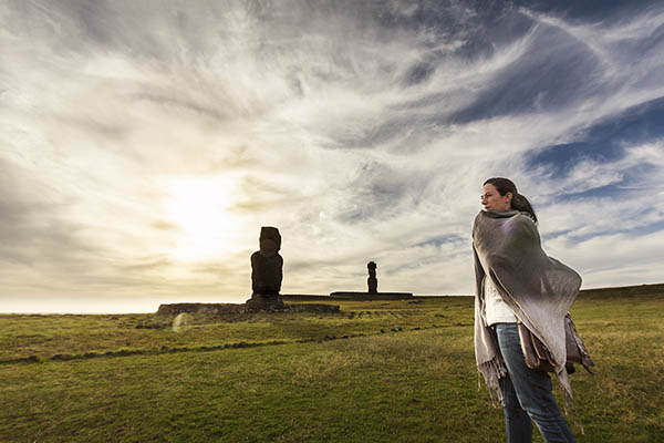 Woman standing in a field on Easter Island with Moai statues in background, Chile