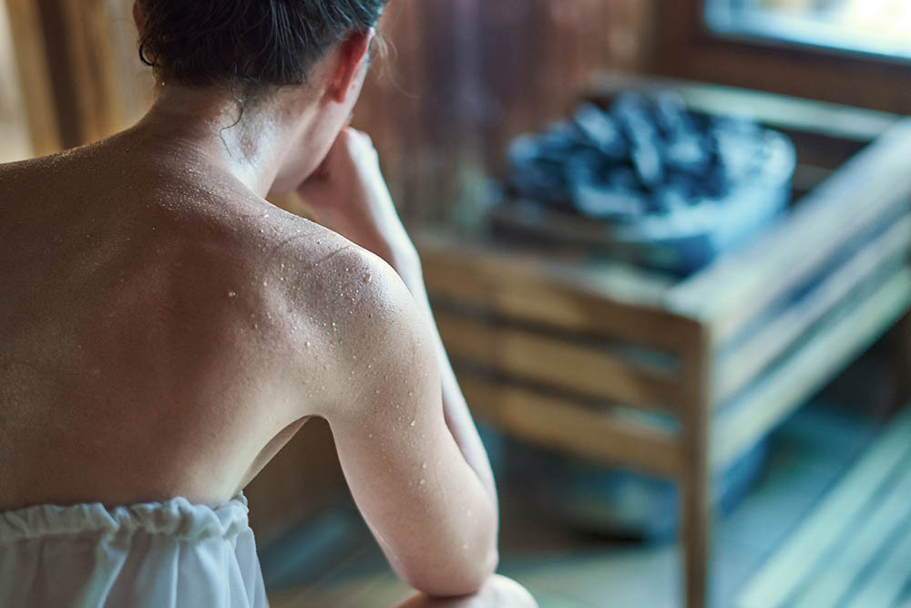 Woman sweating in Finnish sauna, steaming hot stone in the background