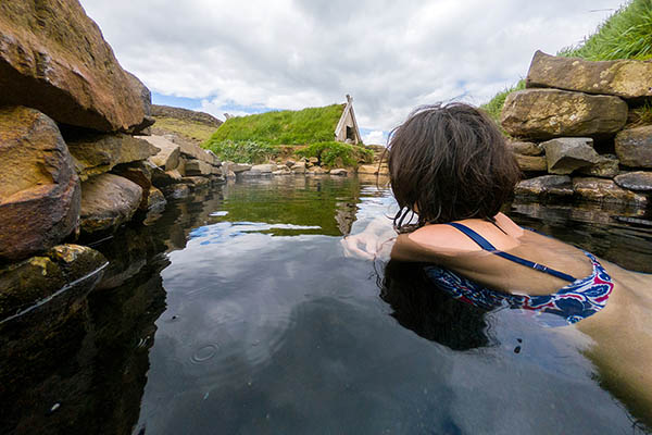 Woman bathing and relaxing in a small hot spring pool in Hrunalaug, Iceland