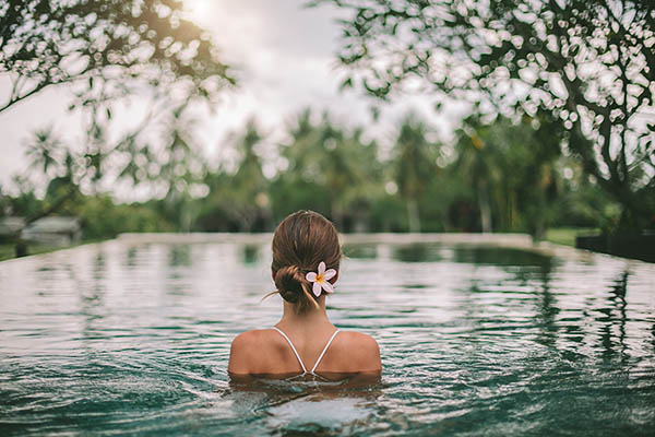 Back view of a young woman in an infinity pool with a view on palm trees, Ubud, Bali, Indonesia