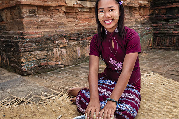 Young Burmese girl with thanaka face paint preparing thanaka paste in the ancient temple of Bagan, Myanmar (Burma)