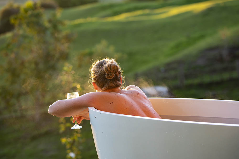 Woman in an outdoor bath with a glass of wine watching the sunset in the Bay of Islands, New Zealand