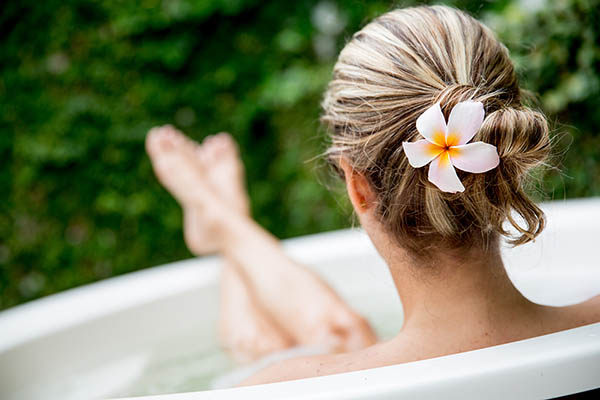 back view of a woman sitting in an out door bath with a flower in her hair