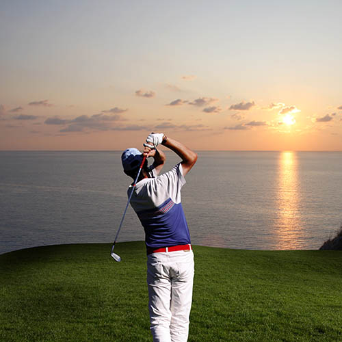 Golfer taking a swing on a golf course by the sea at sunset