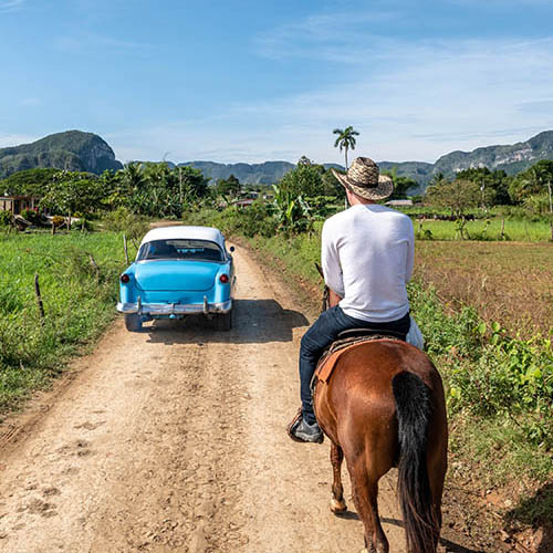 Classic car passes a man on horse in Vinales, Cuba