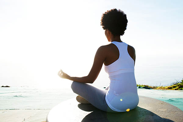 Rear view portrait of young african american woman sitting at beach in yoga pose