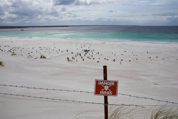 White sandy beach in Yorke Bay, home to a colony of Magellanic Penguins and land mines warning sign, near Stanley, Falkland Islands