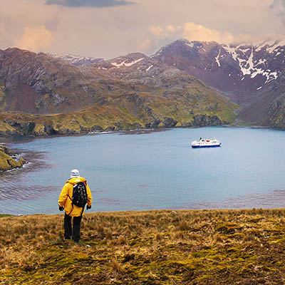 landscape scene of South Georgia Island with Antarctic expedition ship passengers walking back to harbor where ship is anchored