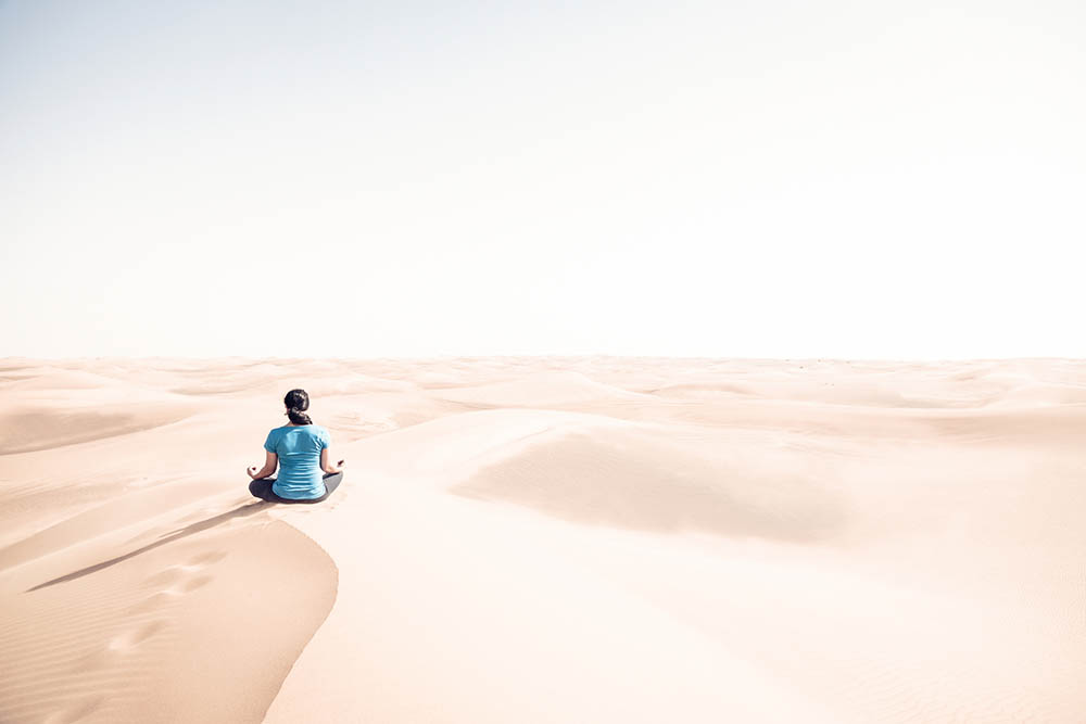 Woman sitting in yoga pose on a sand dune in the desert