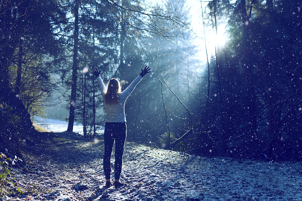 Woman raises her hands and breathing cold air during a sunny winter morning during snowfall. Selective focus used