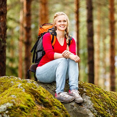 Young woman hiker sitting on a rock while hiking through a forest in Finland