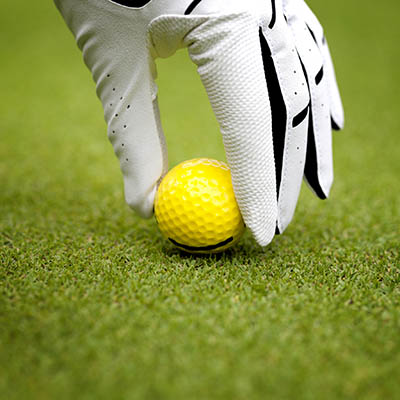 Man`s hand in a white glove putting a golf ball in a golf course 