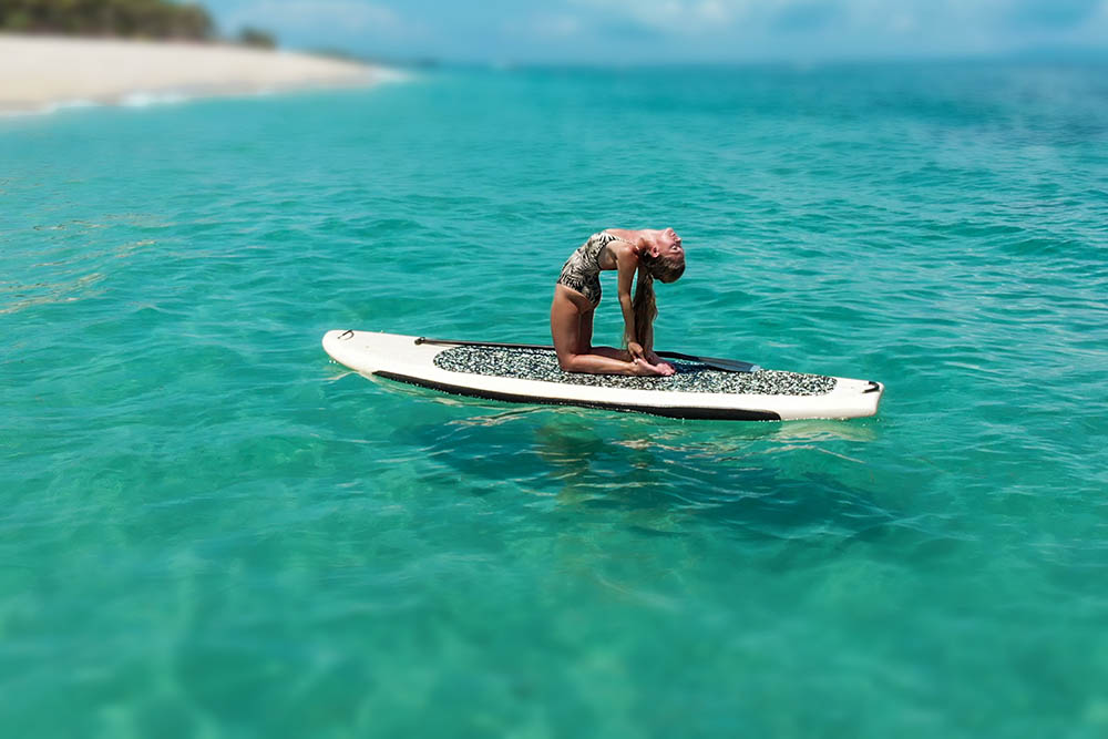 Woman on SUP board in yoga pose off tropical island