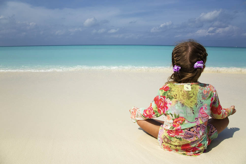 Young girl sitting in a yoga pose on a tropical beach