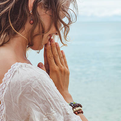 Beautiful young woman praying on the beach