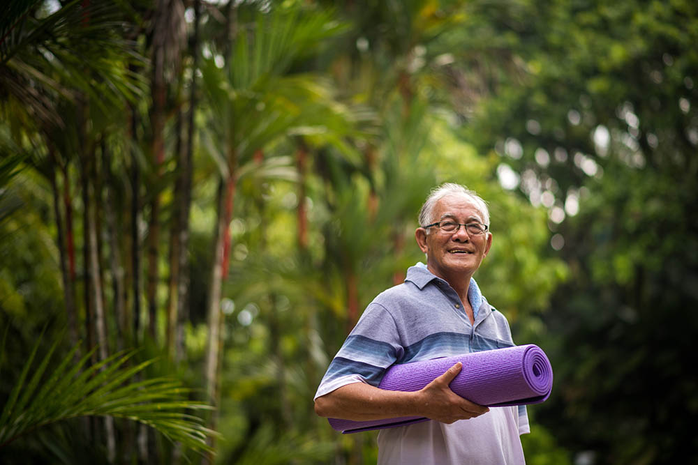 Active senior man holding a yoga mat in the rainforest