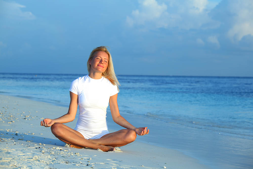 Woman sitting in yoga pose on a beach next to the sea