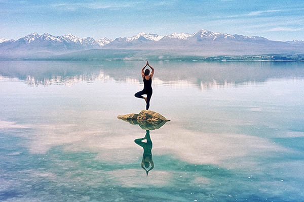 Woman standing in yoga pose in middle of a lake in New Zealand with mountain backdrop