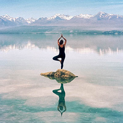 Woman standing in yoga pose in middle of a lake in New Zealand with mountain backdrop