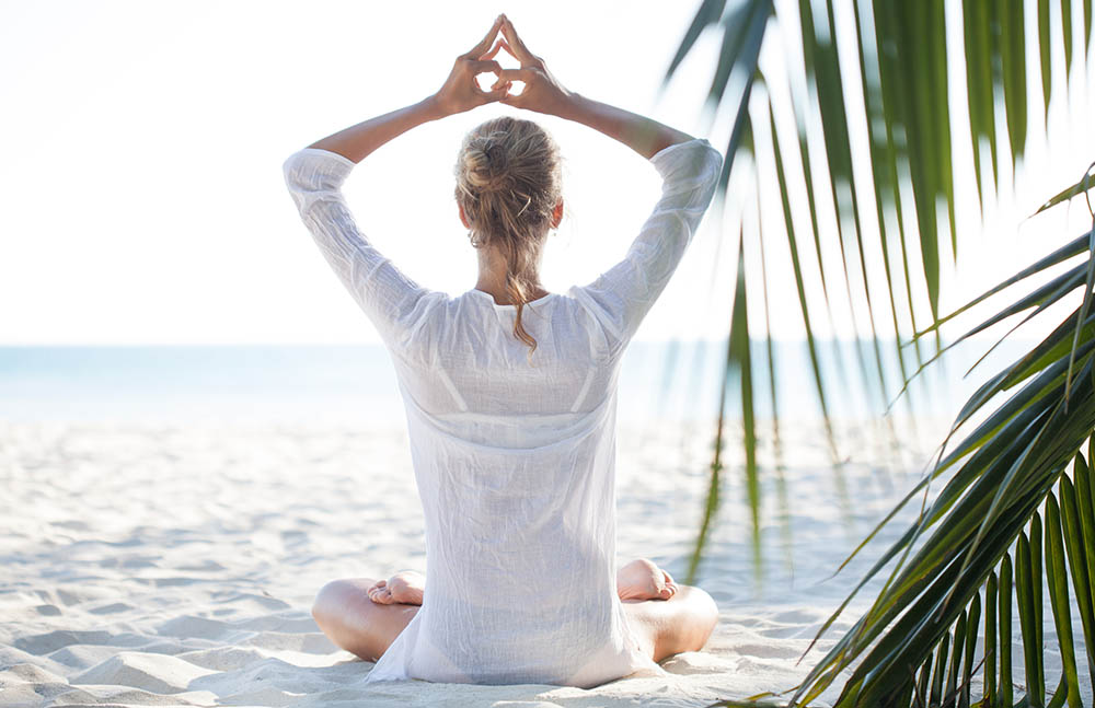 Young woman sitting on the beach and meditating