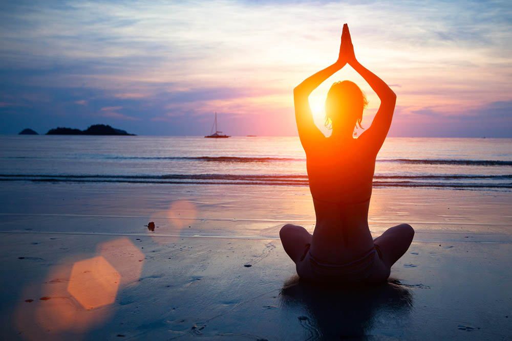 Silhouette young woman practicing yoga on the beach at sunset