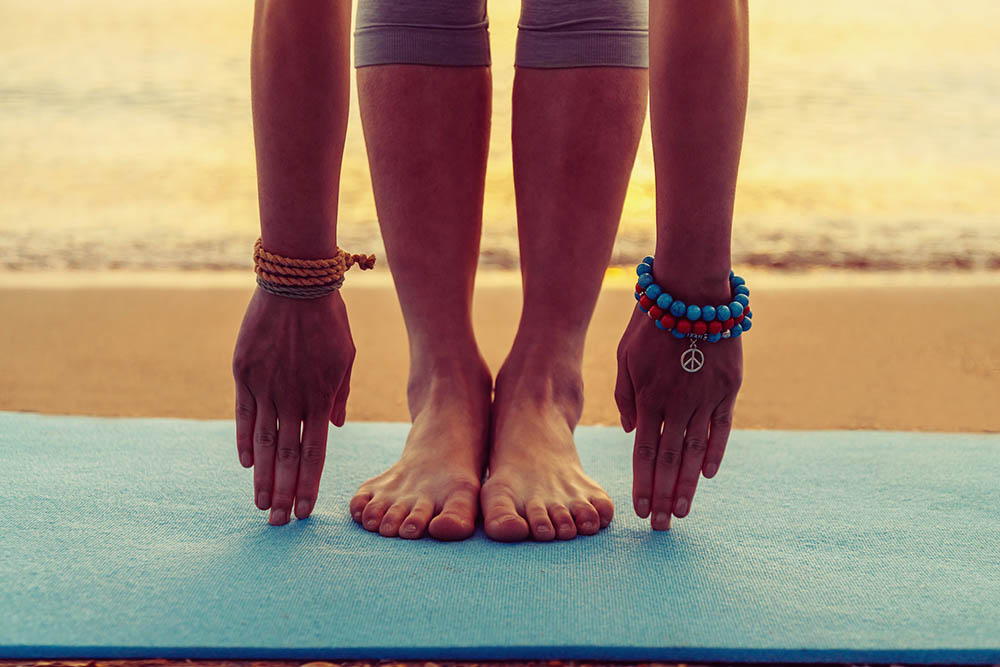 Young woman doing yoga exercise on beach near the sea at sunset in summer, face is not visible