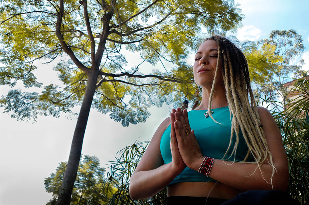 Woman with blonde dreadlocks in meditation posture under a tree